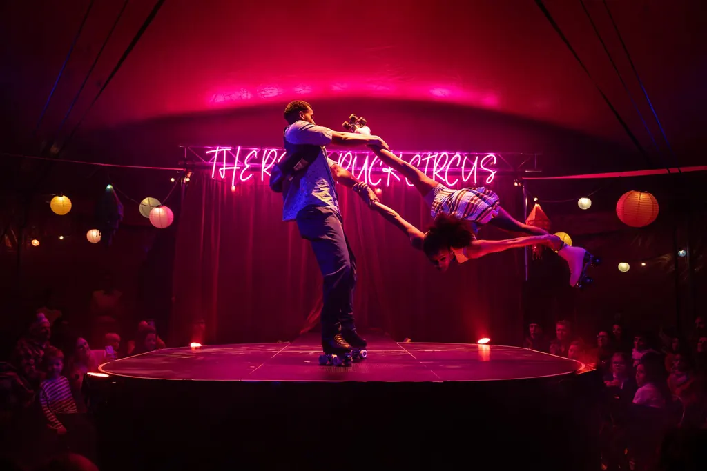 A roller-skating duo spin under the neon Revel Puck Circus sign at Fête du Puck, Walthamstow